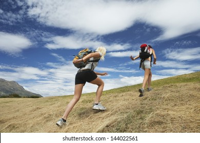 Rear view of two women running up hill against cloudy sky