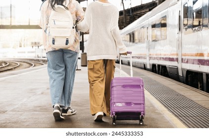 Rear view of two young black women pulling a suitcase and walking together on the platform of a train station to catch a train for a trip. - Powered by Shutterstock