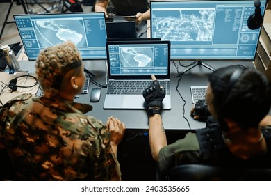 Rear view of two young intercultural male and female officers looking at laptop screen with surveillance camera while one of them making report