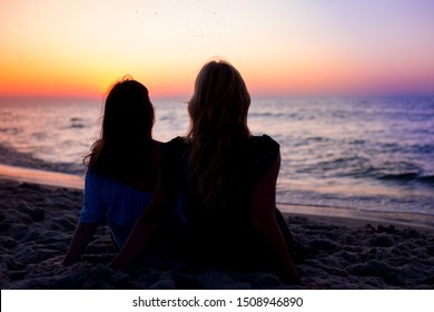 Rear View Of Two Young Women Looking At Sea At Sunset. Silhouettes of two young women watching at beach at colorful sunset - Powered by Shutterstock