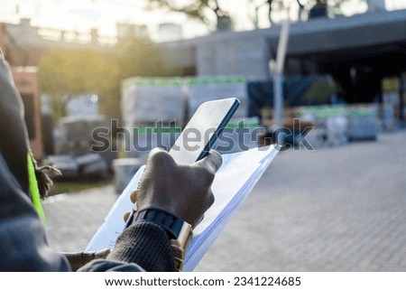 rear view of unrecognizable african ethnicity man standing using phone with construction site in background, industry concept, copy space