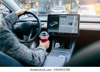 Rear view of unrecognizable female driving modern electric car. Tesla tablet screen.