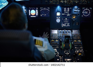 Rear View Of Unrecognizable Pilot Sitting At Control Panel With Radar Devices And Flight System Buttons And Flying Plane On Autopilot