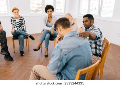 Rear view of unrecognizable sad crying man sharing life problem grief with multiracial women and men. Diverse people consoling hug upset man provide psychological help support on group therapy meeting - Powered by Shutterstock