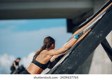 Rear view of an unrecognizable woman athlete partake in one of the events of an obstacle course race while climbing over the wooden wall. Female working out outside. Sport competition and OCR race. - Powered by Shutterstock