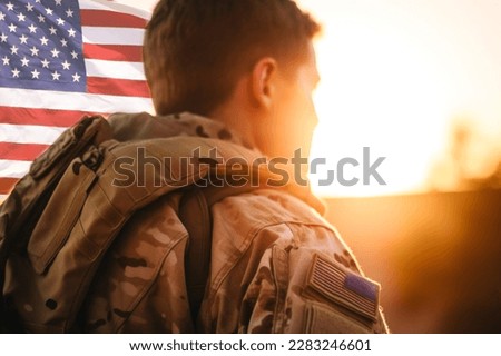 Rear view of a U.S. soldier looking at the sunset and a U.S. national flag.