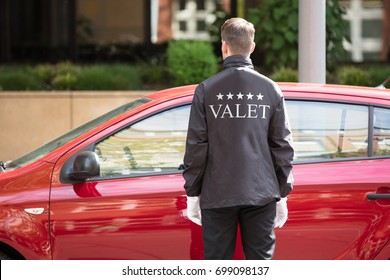 Rear View Of A Valet Standing In Front Of Red Car
