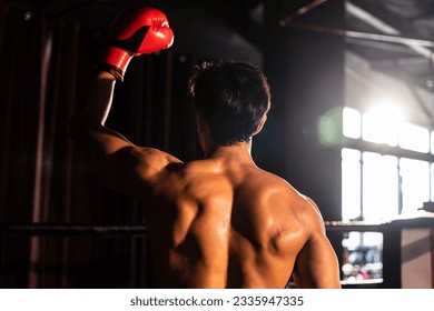 Rear view of the victorious Muay Thai boxer strikes triumphant pose, basking in glory of his hard-earned victory proudly displaying his strong and muscular body. Impetus - Powered by Shutterstock