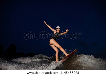 Rear view wakesurfer girl riding on the wakesurf on high wave of motorboat on the background of night sky