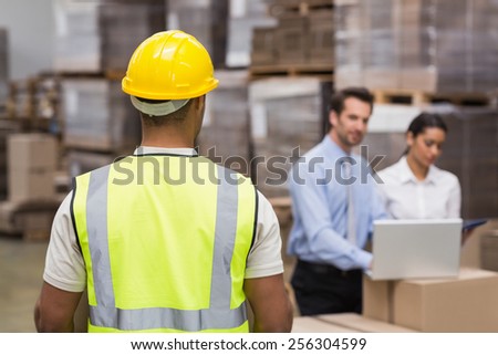 Rear view of warehouse worker in front of his managers in a large warehouse