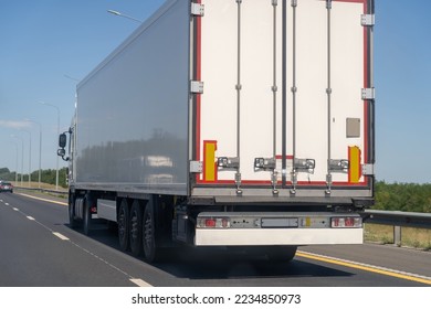 Rear view of white van semi truck drive on suburban asphalted highway road at summer day against blue sky, cargo transportation concept.