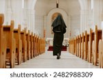 Rear view wide shot of unrecognizable Catholic nun walking along nave towards altar in church, copy space