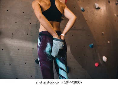 Rear view of woman at applying magnesium chalk powder on hands from a bag tied to her waist. Cropped shot of woman applying gripping powder before climbing boulder wall at a wall climbing gym. - Powered by Shutterstock