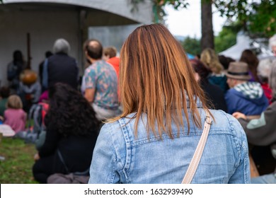 Rear View Of Woman With Audience Listening Kora Lute Music By Musician And Relaxing. Against Tent In Park During World And Spoken Word Event In City