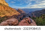 Rear view of woman with backpack sitting on rock along Bright Angel trail with aerial overlook of South Rim of Grand Canyon National Park, Arizona, USA, America. Amazing vista after sunrise in summer