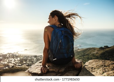 Rear view of a woman with backpack sitting on the cliff and looking at the view Female hiker relaxing on mountain top. - Powered by Shutterstock