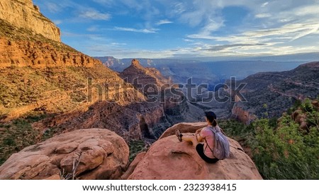 Rear view of woman with backpack sitting on rock along Bright Angel trail with aerial overlook of South Rim of Grand Canyon National Park, Arizona, USA, America. Amazing vista after sunrise in summer