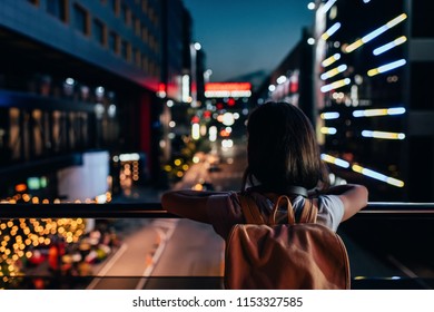 rear view of woman with backpack standing on street and looking at night city lights - Powered by Shutterstock