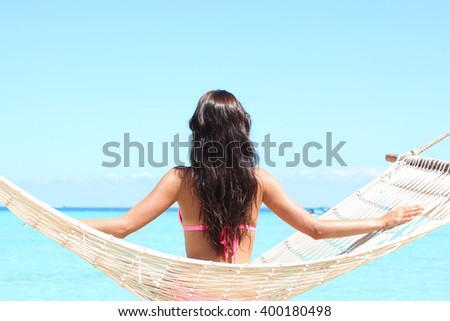 Rear view of a woman in bikini sitting on a hammock on a beach by the sea