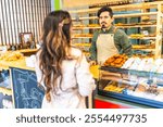 Rear view of a woman buying in an artisan bakery attended by a latin salesman