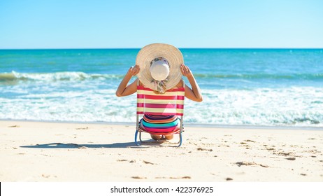 Rear view of woman in chair on summer time sun light beach holiday location. Blue sunny background