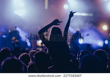 Rear view of a woman in a concert crowd having fun while listening her favorite artist. People having fun at concert.