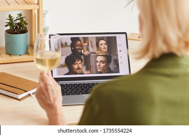 Rear View Of Woman Drinking Wine And Talking Online With Her Friends Using Her Laptop At Home