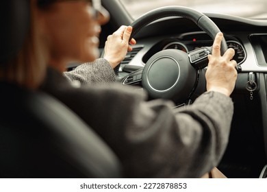 Vista trasera de la mujer que conduce un coche y que lleva ambas manos sobre el volante de dirección en el camino al trabajo