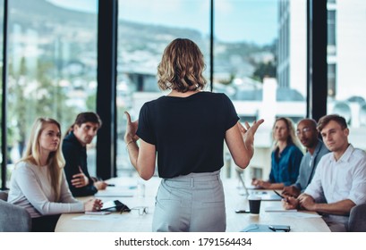 Rear view of a woman explaining new strategies to coworkers during conference meeting in office. Businesspeople meeting in office board room for new project discussion.