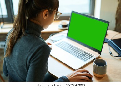 Rear View Woman Freelancer In Eyeglasses Working In Cafe, Using Laptop Computer With A Green Screen On Monitor. Concept Remote Work, Freelance, Working On Laptop Computer Or Net-book.