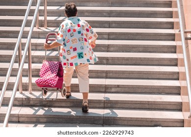 Rear view of a woman with hand grocery trolley carrying it up over stairs. Concept of poor infrastructure for elderly people, just stairs no elevator. - Powered by Shutterstock