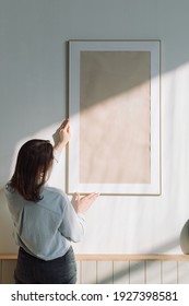 Rear view of a woman hanging a large poster frame on the wall in a modern apartment. - Shutterstock ID 1927398581