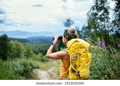 Rear view of woman hiker with backpack on a hiking trip in nature, using binoculars. - Powered by Shutterstock