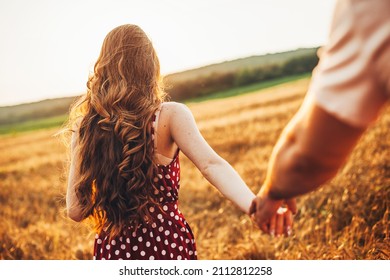 Rear view of a woman with long red hair holding her boyfriend's hand and leading him through the wheat field to the meeting place. For concept design. Wheat