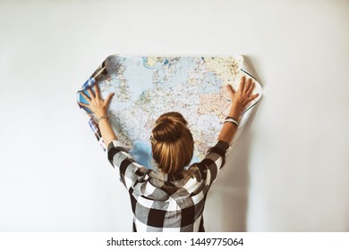rear view of woman looking at map in hands at white brick wall, traveling concept - Shutterstock ID 1449775064