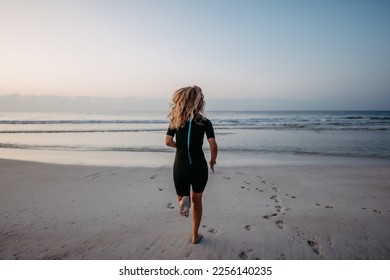 Rear view of woman in neoprene running in to ocean. - Powered by Shutterstock