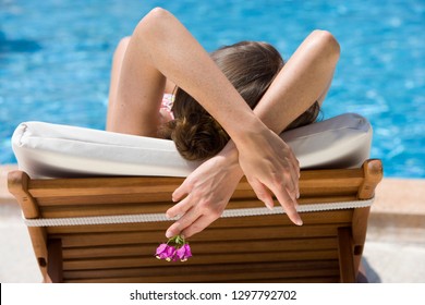 Rear view of woman on holiday holding pink flower relaxing on lounge chair by swimming pool - Powered by Shutterstock