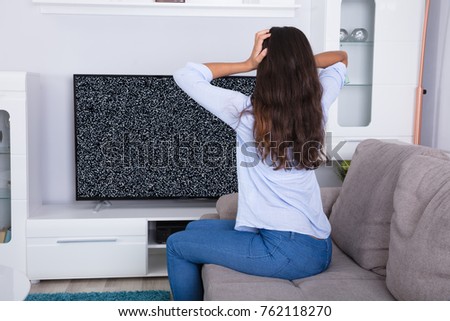Rear View Of A Woman On Sofa Getting Frustrated With Glitch TV Screen At Home