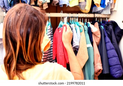 Rear View Of Woman Organizing Clothes In Her Children's Closet. Season Clothes. Season Change