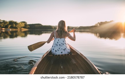 Rear view of woman paddling the canoe on sunset lake