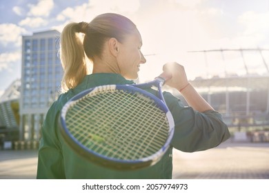 Rear view of woman, professional tennis player walking with tennis racket outdoors, ready for morning workout