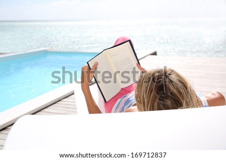 Rear view of woman reading novel by the sea
