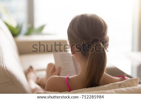Rear view at woman reading open paper tome on couch at home, young book lover spending leisure time enjoying new bestseller novel on sofa, teenager reviewing literature included to student course