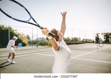 Rear view of a woman serving the ball while playing a mixed doubles tennis match. Men and women playing tennis outdoors on a sunny day.