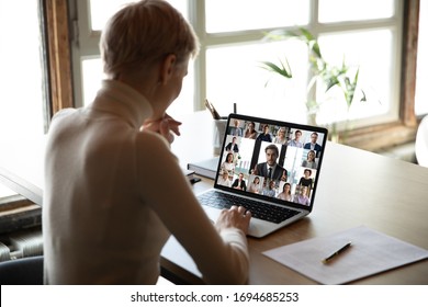 Rear view woman sit at desk learns new videoconference app online review, look at pc screen take part in group video call with corporate staff brainstorm distantly, study, work use modern tech concept