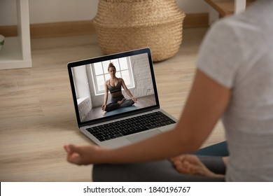 Rear view of woman sit on floor practice yoga watching class or training on laptop from home online. Female engaged in webcam meditation practice on computer, do sports on internet with instructor.