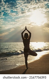 Rear View Of A Woman Standing In A Tree Position On The Seashore. She's Watching The Sun. Inner Harmony And Self Body Care.