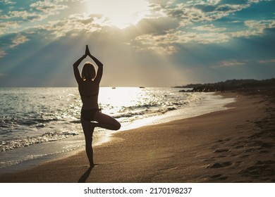 Rear View Of A Woman Standing In A Tree Position On The Seashore. She's Watching The Sun. Inner Harmony And Self Body Care.