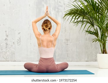 Rear view of a woman in the Sukhasana yoga pose seated in the lotus position with hands raised in prayer while meditating