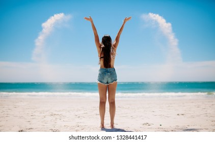Rear view of a woman throwing sand in air making a illusionary heart shape. Woman having fun at the beach playing with sand facing the sea.